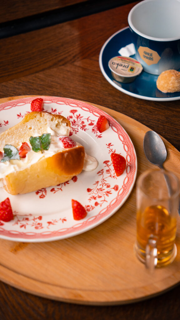 Une vue sur la table dressée avec une assiette de Baba au rhum servi avec de la crème fraîche et des fraises, et accompagné d'un verre de vin de dessert italien