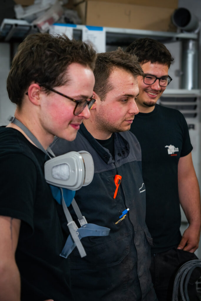 Trois mécaniciens du garage Frambach regardent vers la droite en souriant