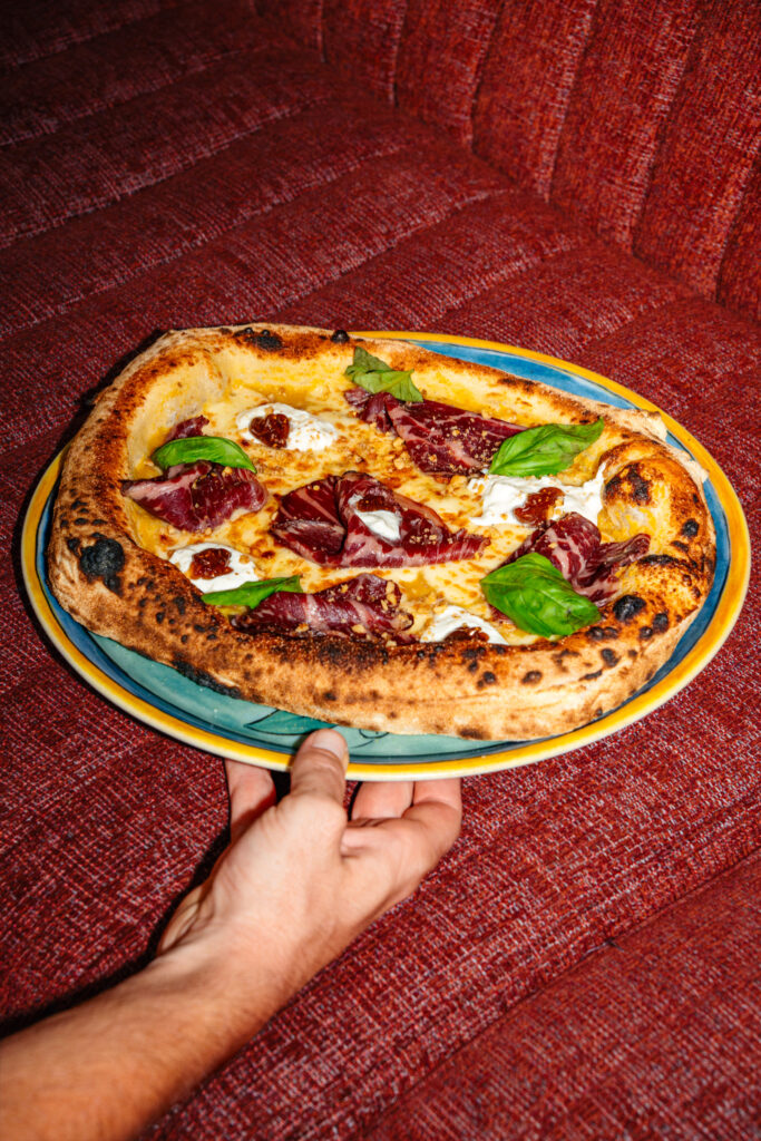Une main tenant une assiette avec une pizza de menu de suggestion, base tomates jaune, jambon italien et stracciatella