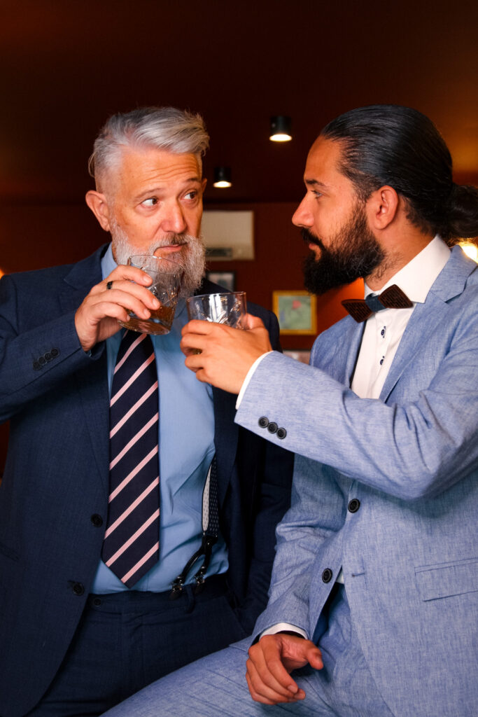 Marco et Simon trinquent en se regardant dans les yeux, tous les deux habillés en costume classique