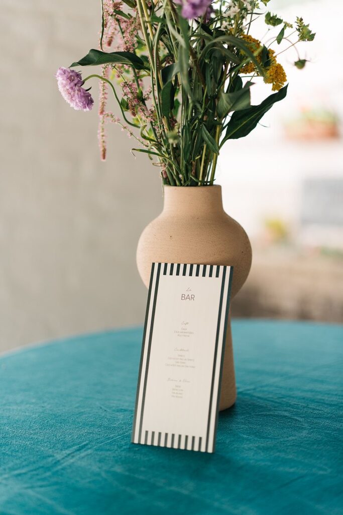 Menu bar posé contre un vase rempli de fleurs sur une table vert forêt