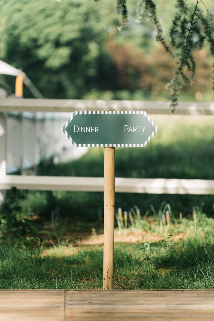 Un panneau de signalétique indiquant le "dinner" à gauche et la "party" à droite, un jardin flouté dans le fond